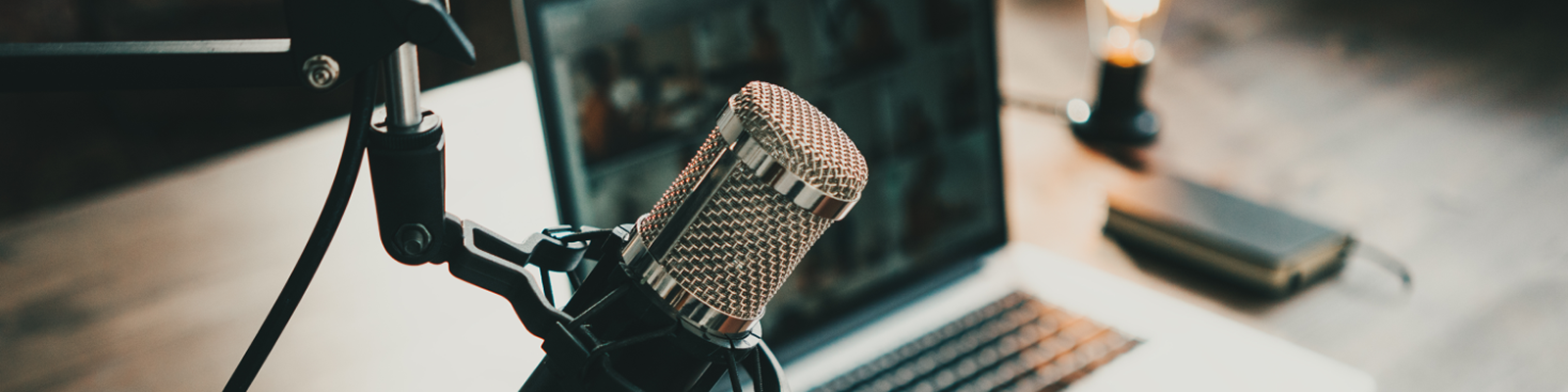 Image shows a microphone on a boom with a laptop with a person creating a podcast